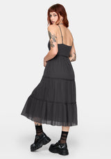 Woman wearing a grey midi dress with tattoos on arms and neck against a white background