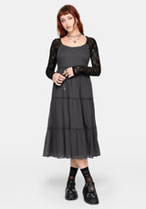 Woman wearing a grey midi dress with a black lace long sleeve top underneath and black Mary Janes.