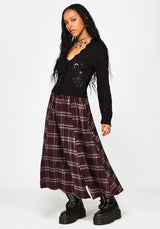 A model wearing a black long-sleeve jumper with celestial embroidery and a long burgundy plaid skirt, paired with black combat boots, against a plain white studio background.