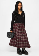 A model wearing a black knit cardigan with moon and star embroidery, a burgundy and gray plaid midi skirt, and black combat boots, holding a small black handbag against a light gray background.