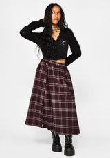 A model wearing a black long-sleeve crop top with moon and star embroidery, paired with a high-waisted burgundy and black plaid midi skirt and black platform combat boots, against a plain light gray background.