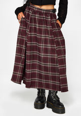 A person wearing a pleated A-line skirt in a burgundy and gray plaid pattern, styled with a black crop top and black combat boots against a light gray background.