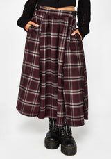 A person wearing a long pleated plaid skirt in burgundy, black, and white, paired with black platform boots and a black cropped top, shown against a light gray studio background.