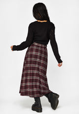 A model shown from behind wearing a black long-sleeve knit top and a dark red/burgundy plaid midi skirt with white stripes, paired with black boots, against a plain white studio background.