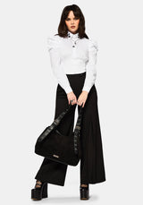 Woman wearing a white blouse and black wide leg trousers holding a black handbag on a white background