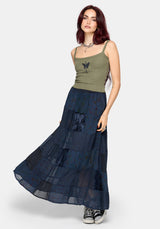 Woman wearing a khaki sleeveless vest with thin straps, cropped length and blue butterfly embroidery in center with a blue patchwork maxi skirt and converse shoes against a white studio background