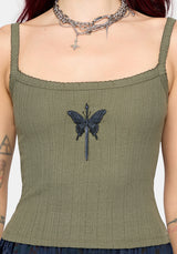 Woman wearing a khaki sleeveless vest with thin straps, cropped length and blue butterfly embroidery in center against a white studio background