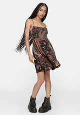 A woman modeling a sleeveless mini dress with a bohemian paisley pattern in black, rust red, and beige, paired with black combat boots against a light gray background.