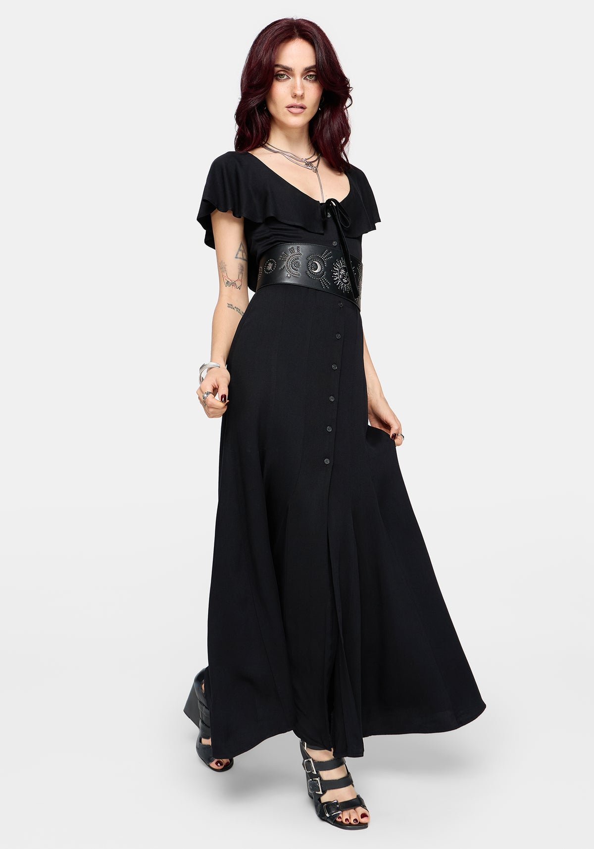 Woman wearing a black maxi dress with frilly short sleeves and a chunky waist belt on a white background