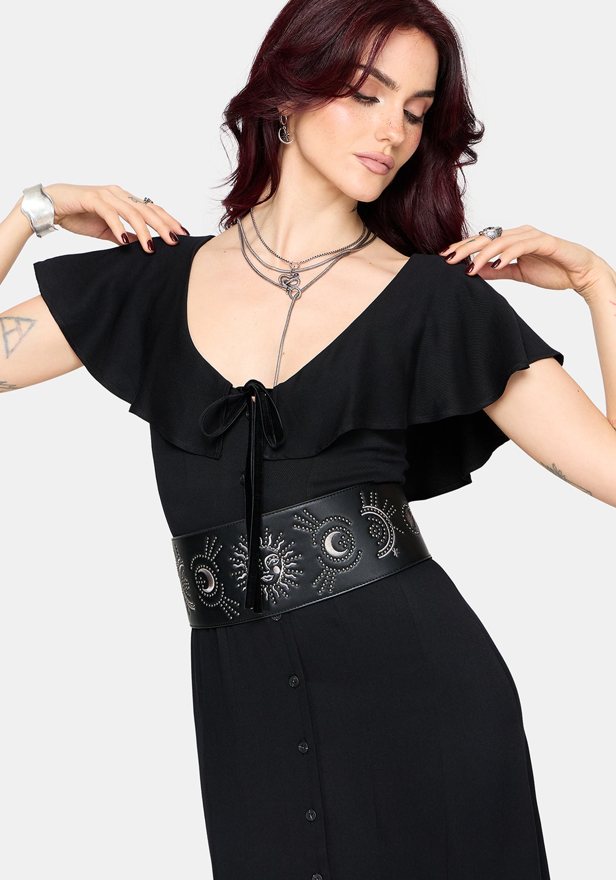 Woman wearing a black maxi dress with frilly short sleeves and a chunky waist belt on a white background