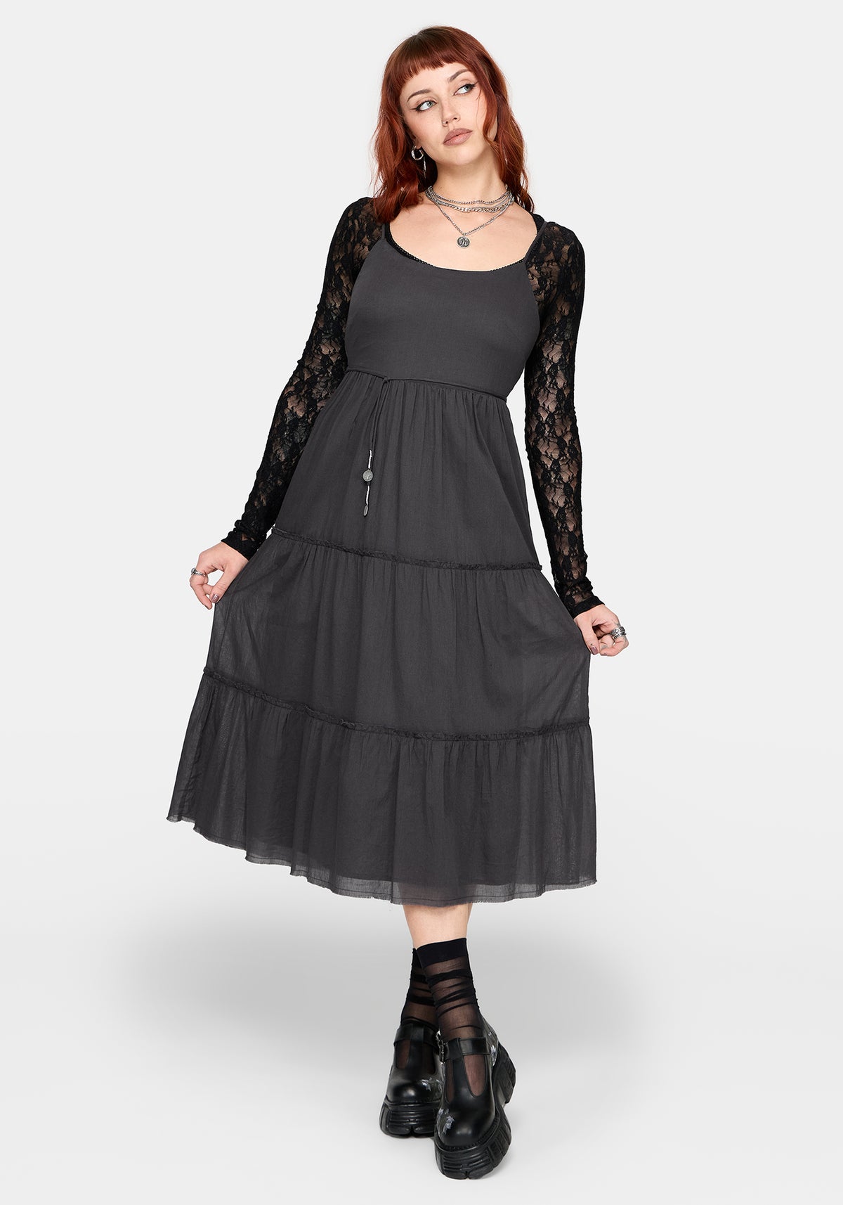 Woman wearing a grey midi dress with a black lace long sleeve top underneath and black Mary Janes. 