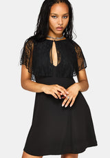 A woman modeling a black dress with sheer lace flutter sleeves, a keyhole cutout at the neckline, and a flared skirt, photographed against a light gray studio background.