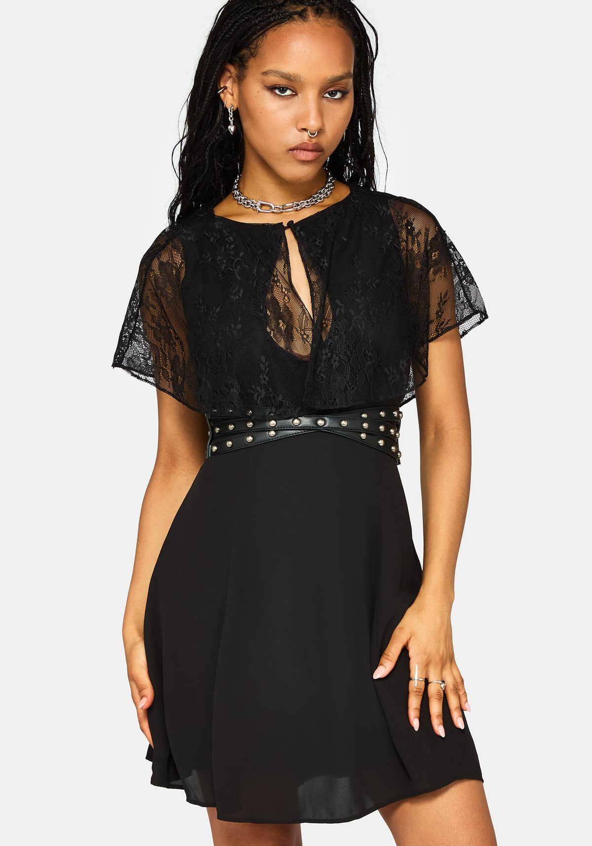 A woman modeling a black lace and chiffon mini dress with a studded waistband, against a light gray background.