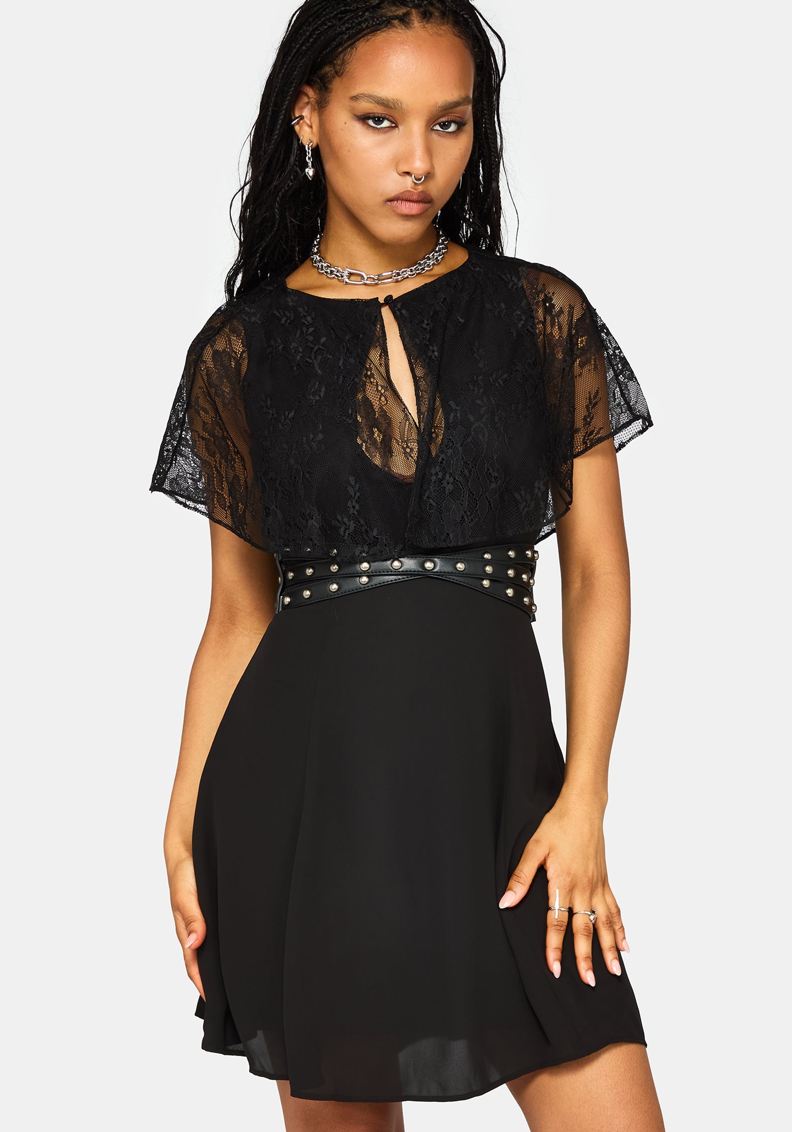 A woman modeling a black lace and chiffon mini dress with a studded waistband, against a light gray background.