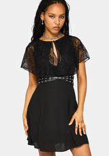 A woman modeling a black lace and chiffon mini dress with a studded waistband, against a light gray background.