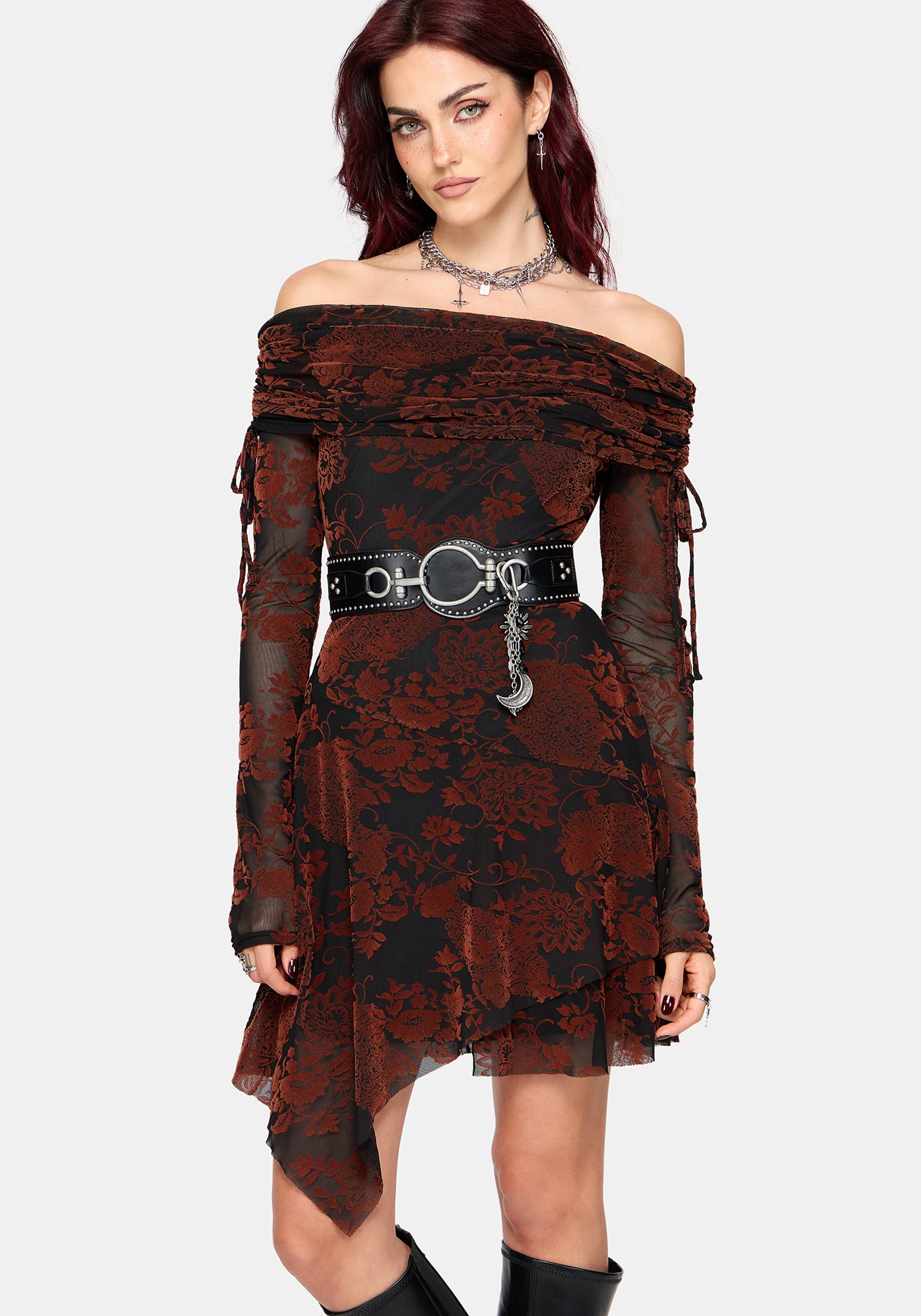 A model wearing a gothic off-the-shoulder mini dress with a dark red and black floral lace pattern, a wide black waist belt with silver hardware and charms, and black boots, set against a plain light gray background.