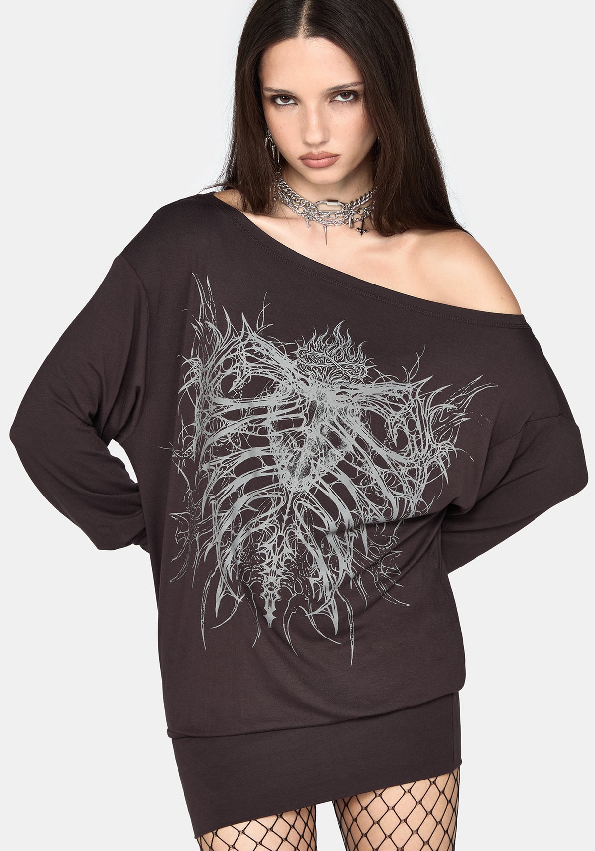 A woman modeling an oversized off-the-shoulder black sweatshirt dress with a large white skeleton rib cage graphic on the front, paired with fishnet tights and a silver choker against a light gray background.