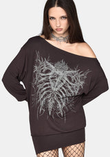 A woman modeling an oversized off-the-shoulder black sweatshirt dress with a large white skeleton rib cage graphic on the front, paired with fishnet tights and a silver choker against a light gray background.