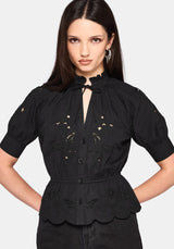 Woman wearing a black blouse with intricate designs on a plain background
