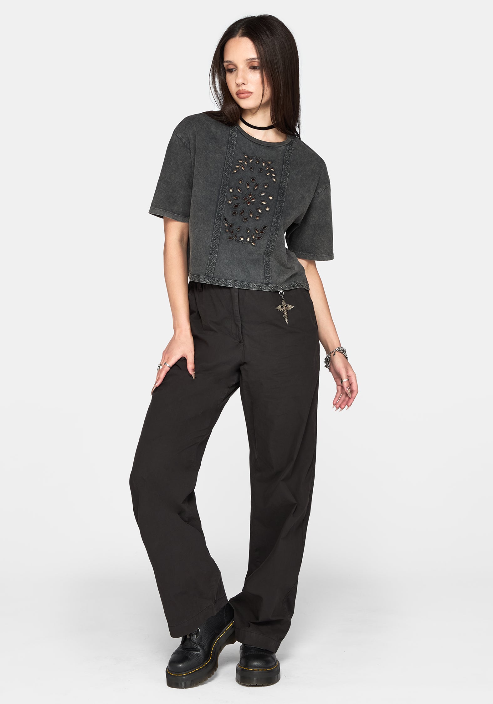 A model wearing a washed charcoal cropped t-shirt with a skull graphic and black wide-leg pants, standing against a light gray studio background.