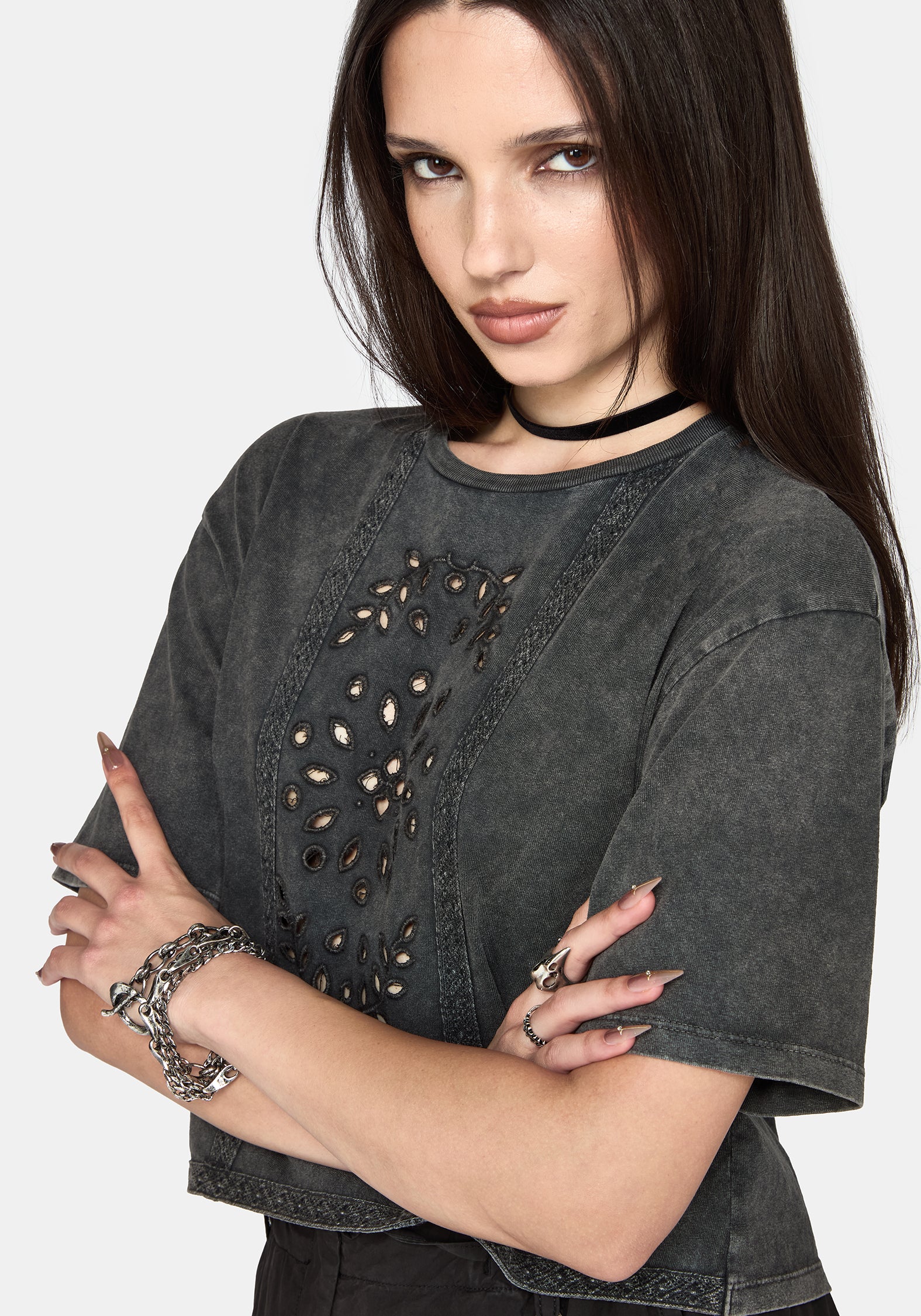 A woman wearing a dark gray washed short-sleeve crop top with cutout details on the front, styled with a black choker and silver bracelets against a light gray background.