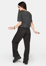A woman posing from the back wearing a dark gray cropped t-shirt and black wide-leg trousers against a light gray background.